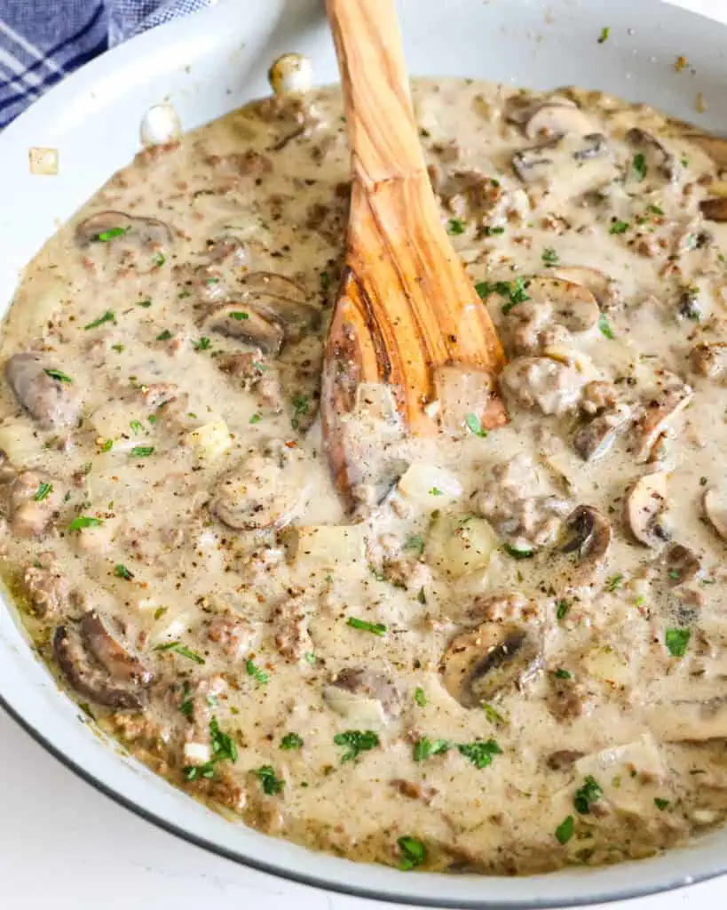 A large skillet full of ground beef stroganoff with a wooden spatula in it. 