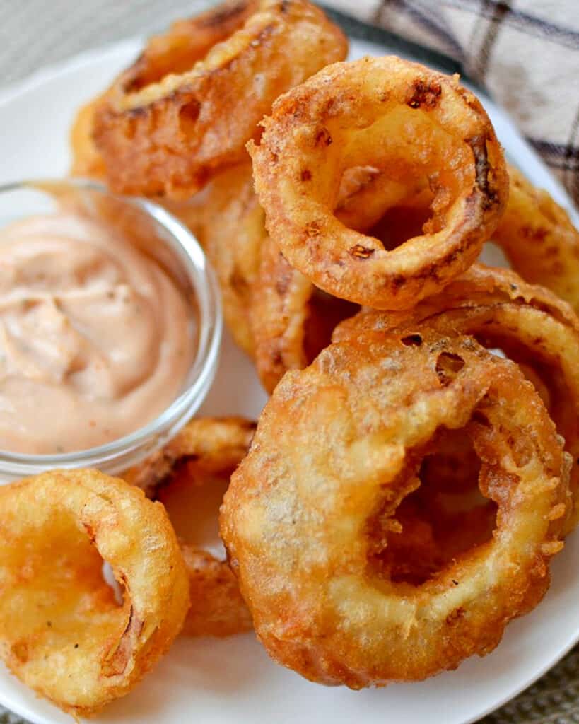 Crispy onion rings on a plate with a small bowl of lime mayo sauce. 