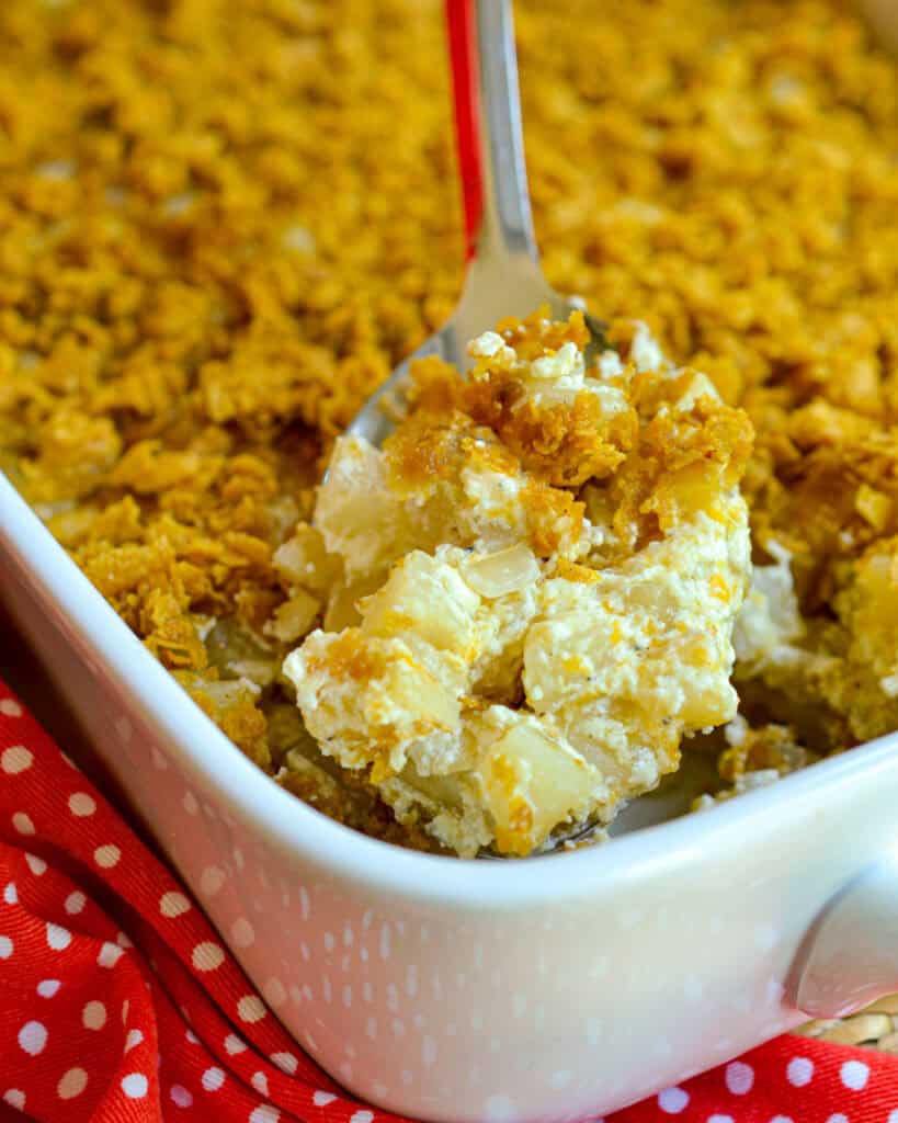 A casserole and large serving spoon full of funeral potatoes. 