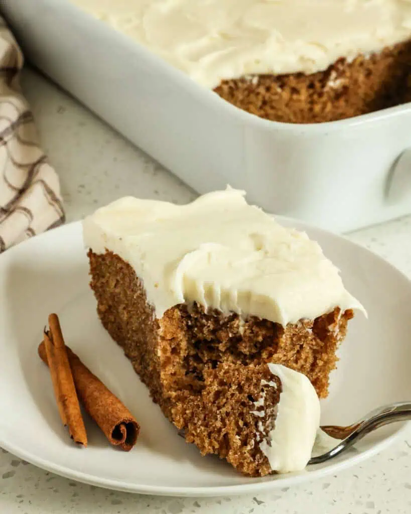 A fork full of spice cake with cream cheese frosting and the rest of the piece in the background. 