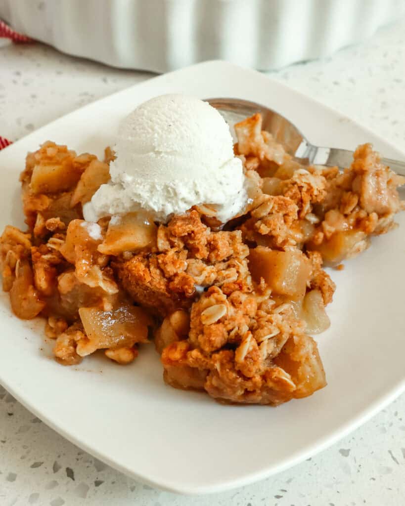 Apple crisp on a single several plate topped with vanilla ice cream. 