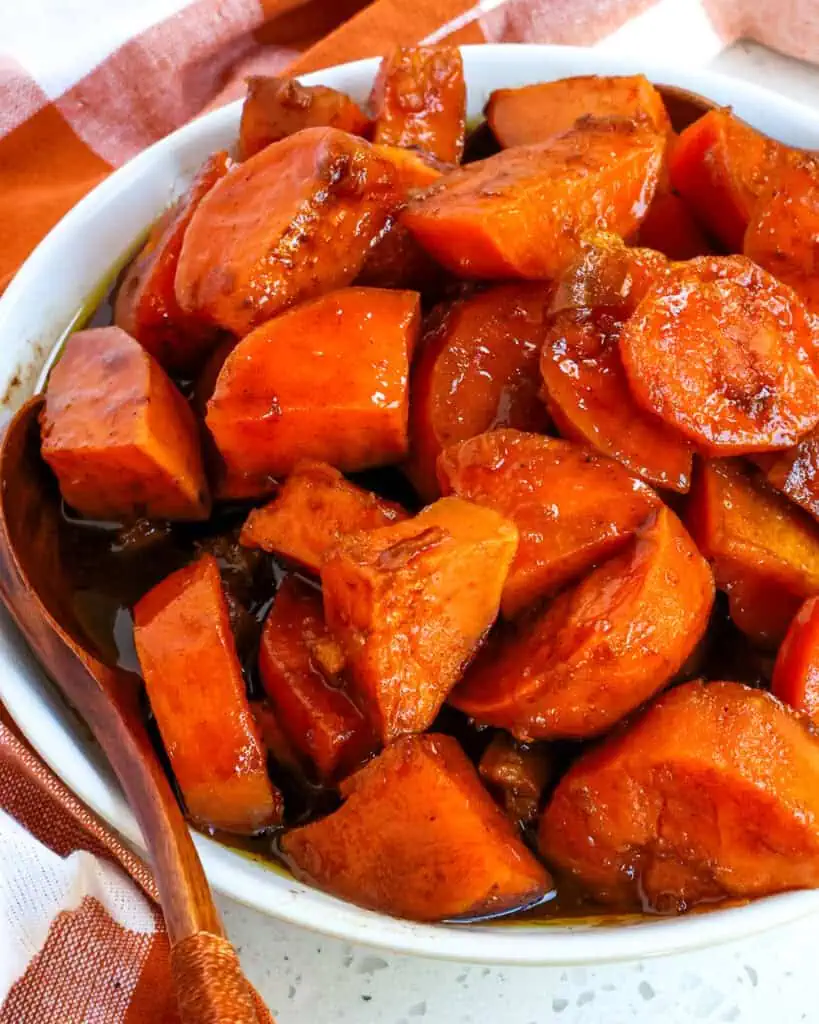 Candied yams in a serving bowl with two wooden spoons. 