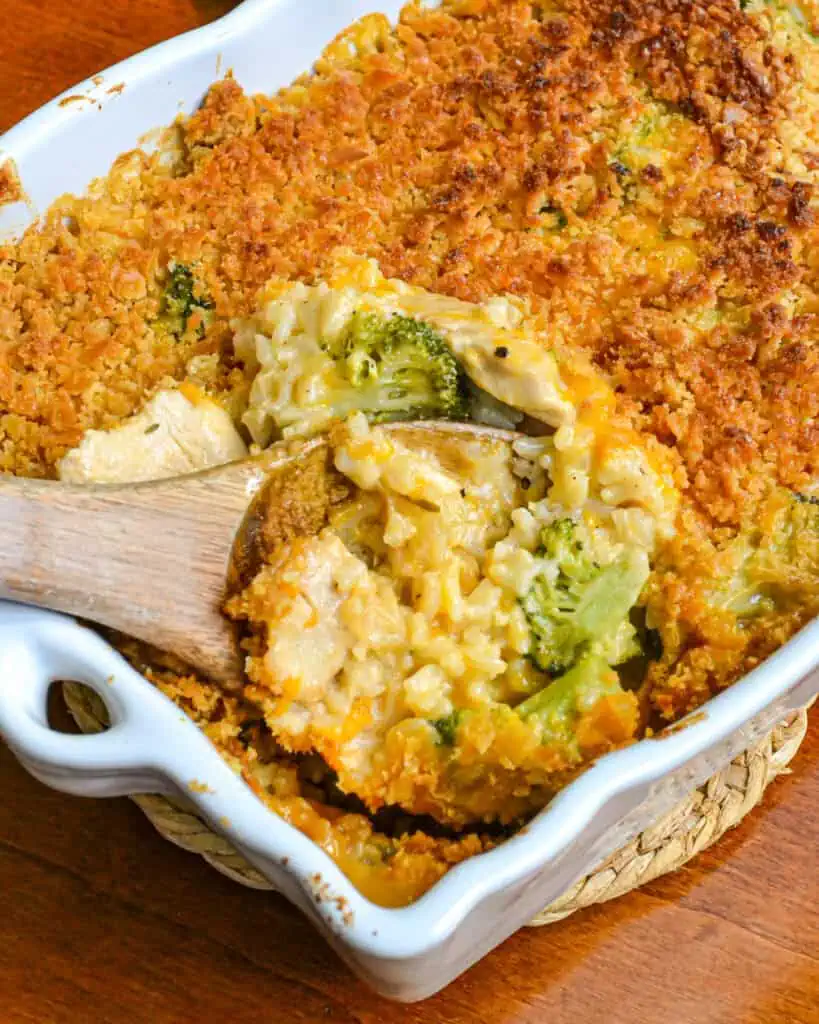 A casserole and a wooden spoon full of chicken broccoli rice casserole. 