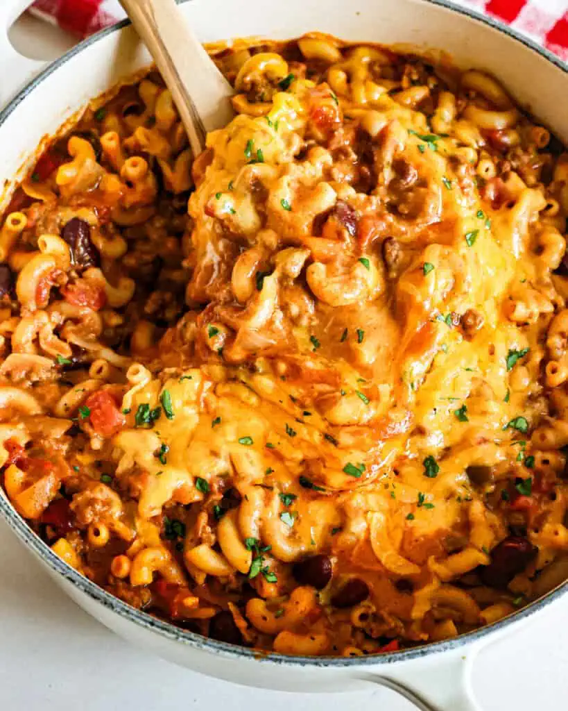 A Dutch oven full of cheesy chili mac garnished with fresh chopped parsley. 