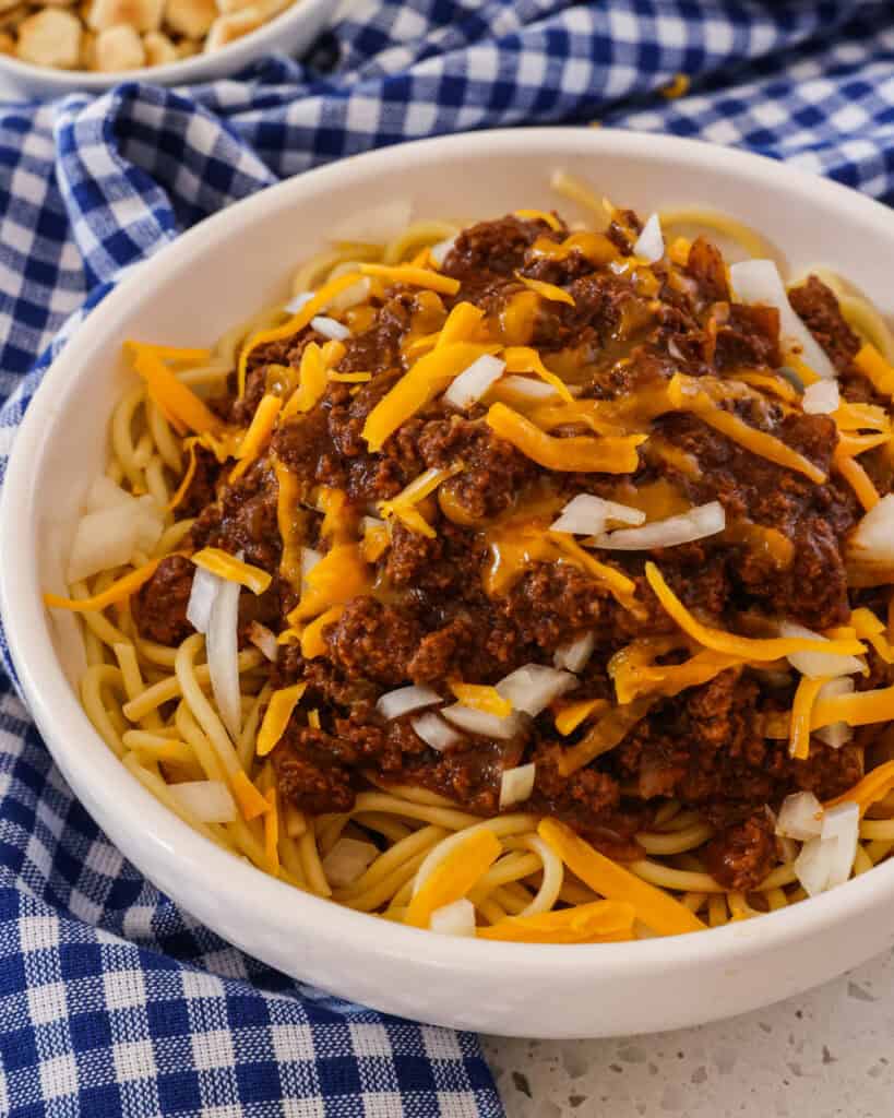 A bowl full of Cincinnati chili over spaghetti and topped with shredded cheddar and onions. 