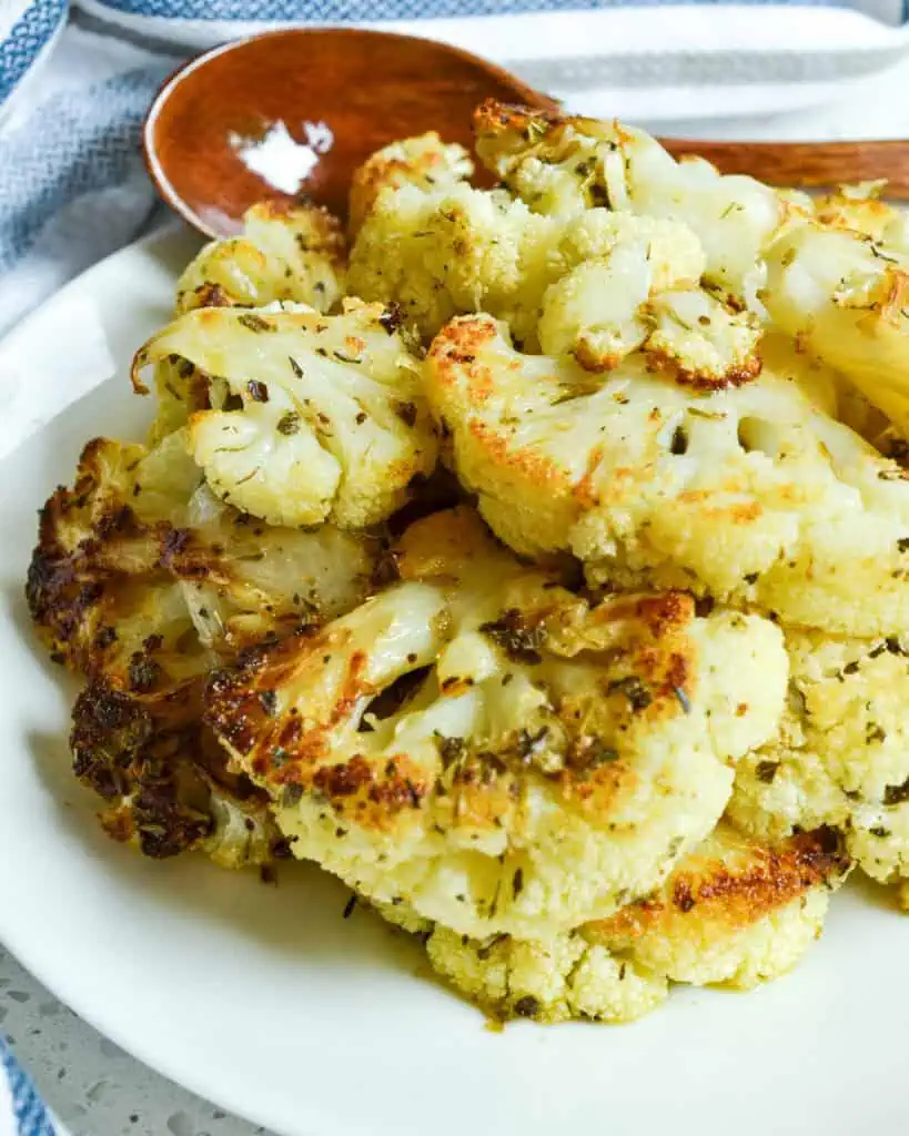 A serving plate and a wooden spoon full of freshly rosted cauliflower. 