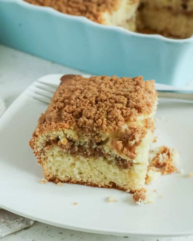 A side view of sour cream coffee cake on a serving plate with a fork. 