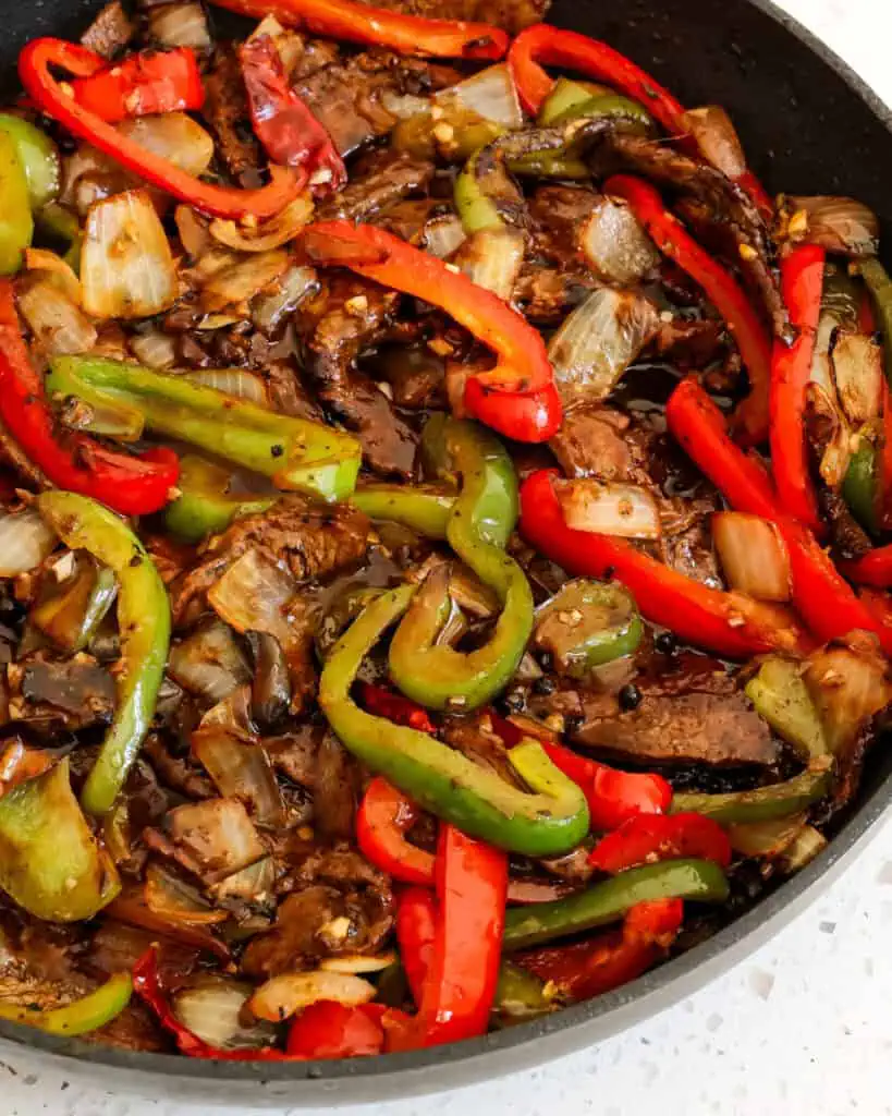 A skillet full of szechuan beef with marinated flank steak with tender-crisp bell peppers, onions, garlic, and ginger in a spicy and savory sauce seasoned with Szechuan peppercorns 