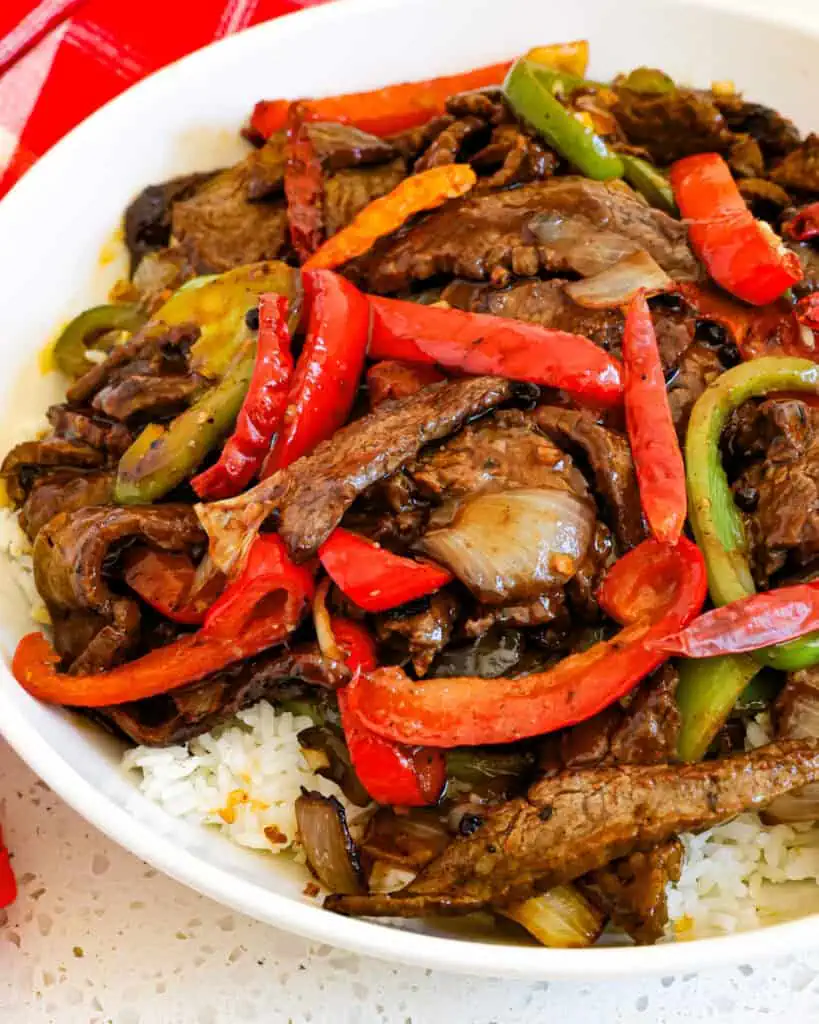 A close up view of szechuan beef over white rice in a bowl. 