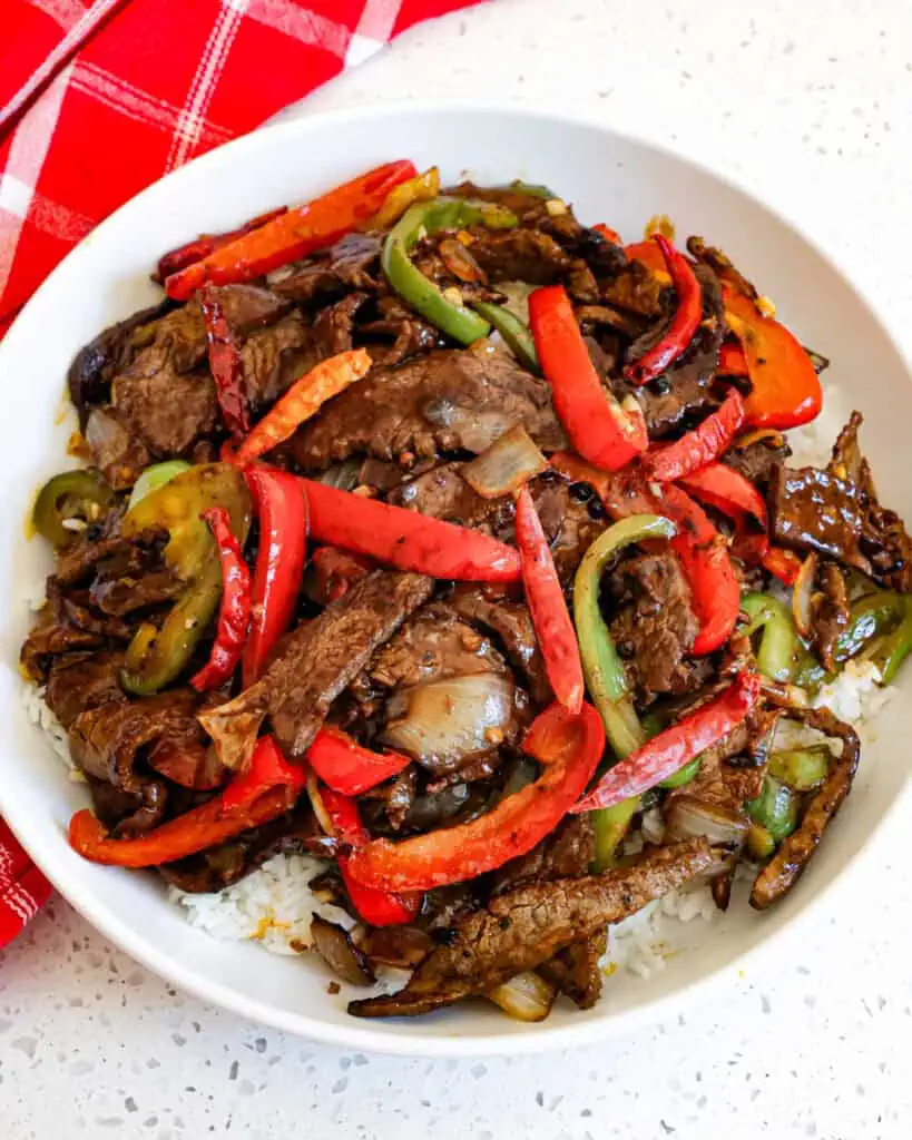 Szechuan beef over white rice on a single serving plate. 