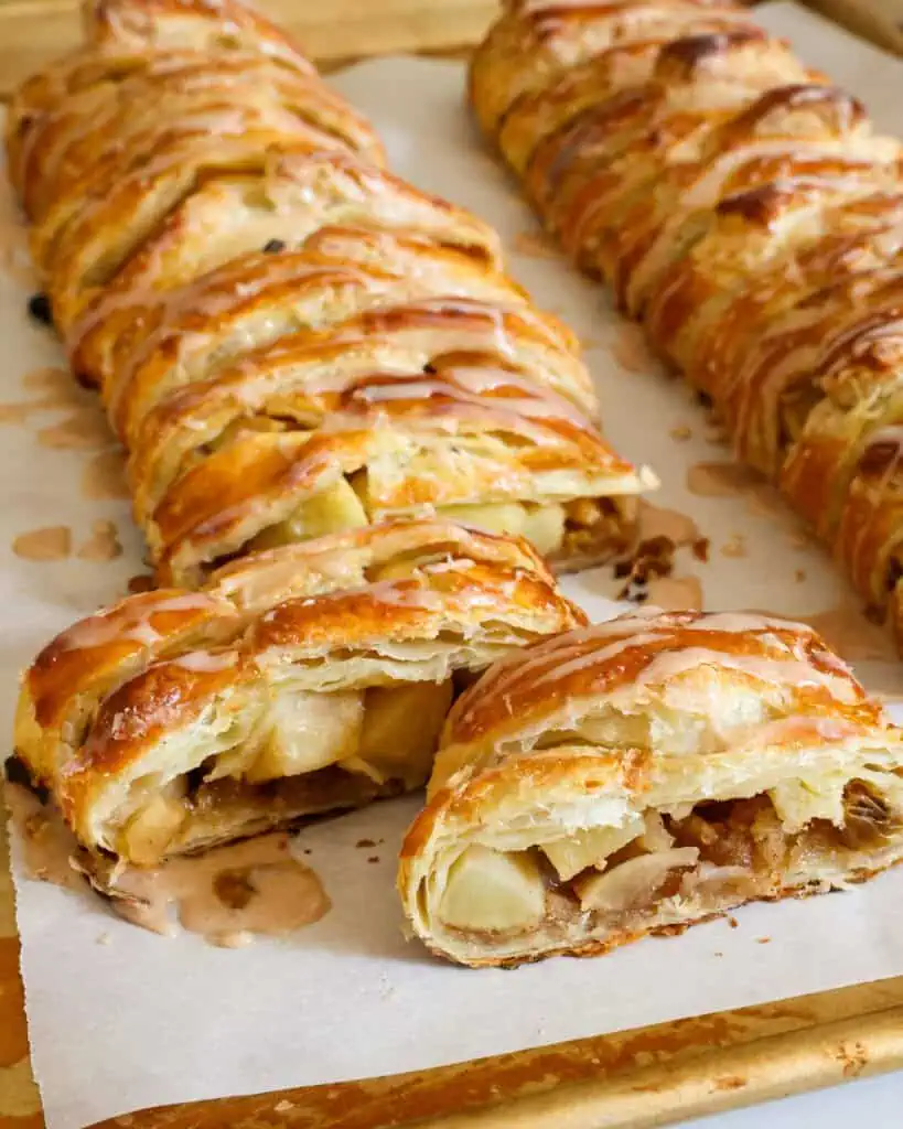 Slices of apple strudel from two strudels on parchment paper on a baking sheet. 