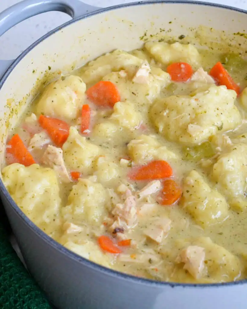 A Dutch oven full of chicken and dumpling soup with carrots, onions, and celery. 