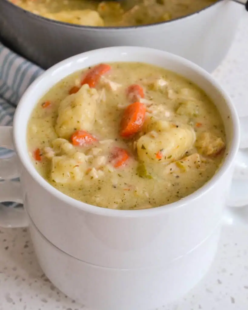 A double stack of white soup crocks with the top crock full of chicken dumpling soup. 