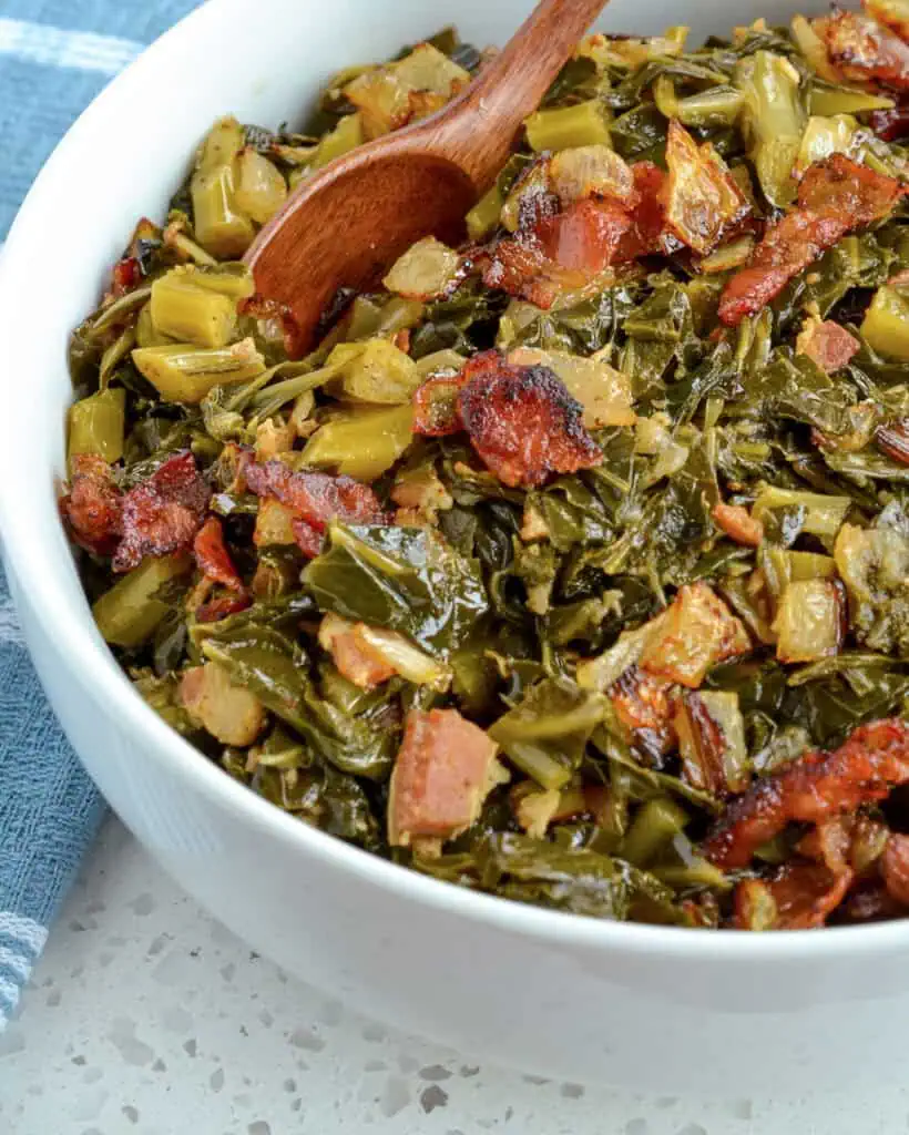 A serving bowl full of collard greens with a wooden spoon in it. 