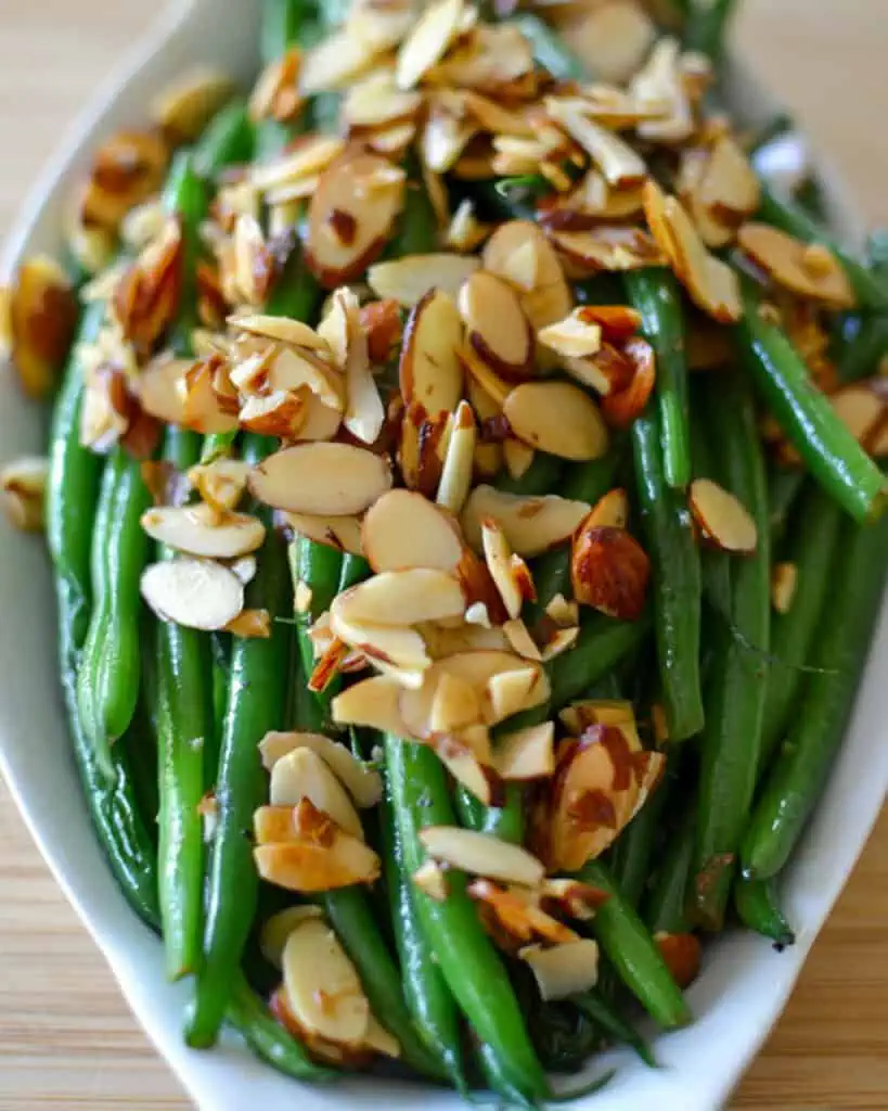 A small serving dish full of green beans almondine. 