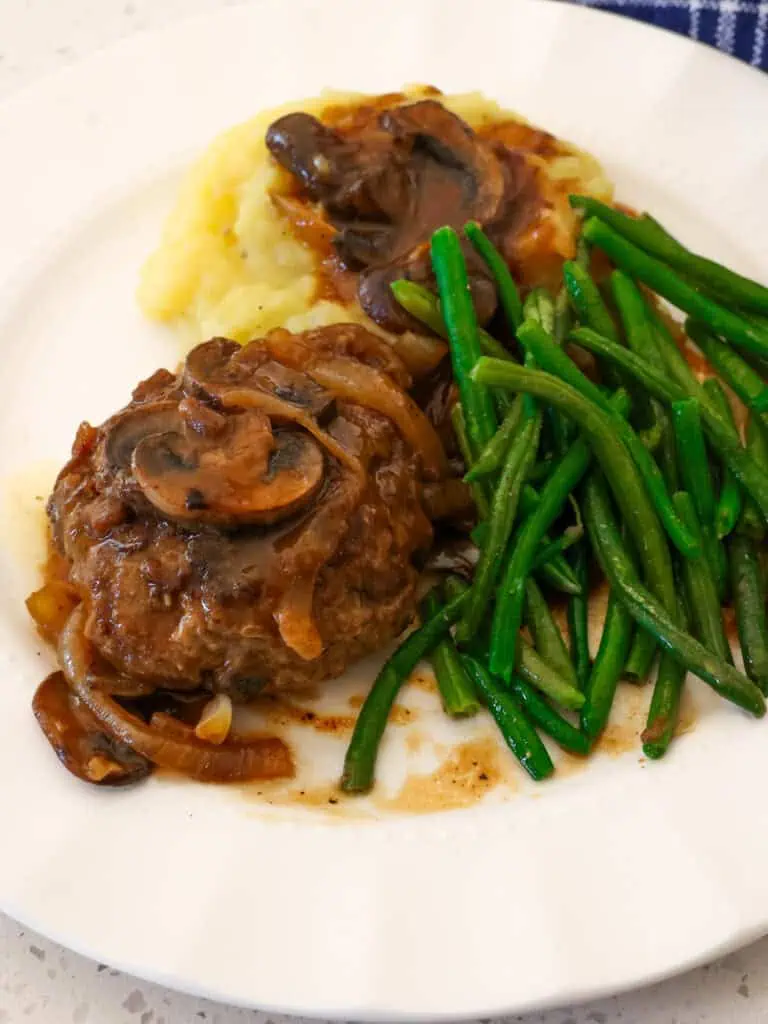 Hamburger steak with green beans, and mashed potatoes on a serving plate. 