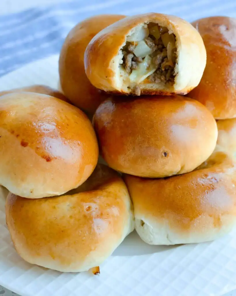 Runzas stacked on a plate with a bite  taken out of one of them. 