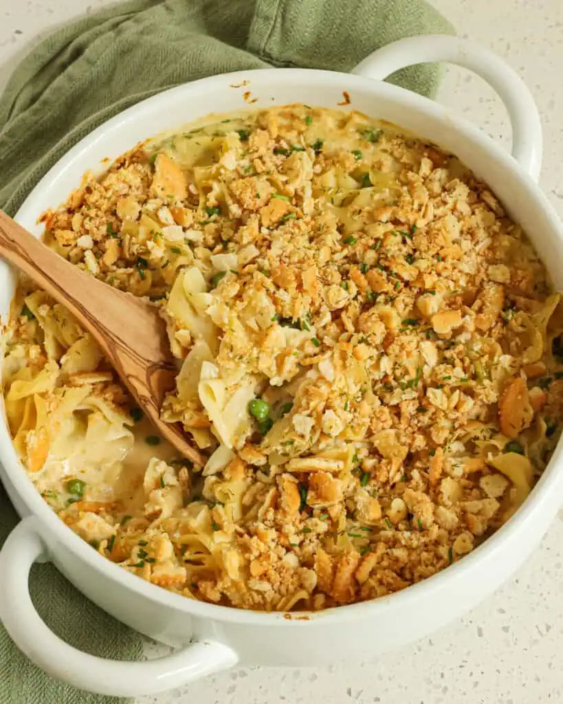 An overhead view of a casserole dish full of tuna noodle cassserole with a wooden spoon in it. 