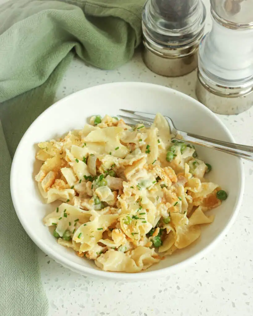 Tuna noodle casserole in a single serving bowl with a fork. A salt and pepper shaker are in the background. 
