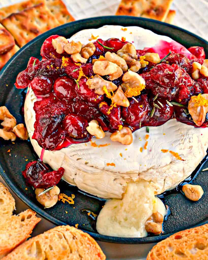 Overhead view of baked brie with cranberries and walnuts on a mini cast iron skillet. 