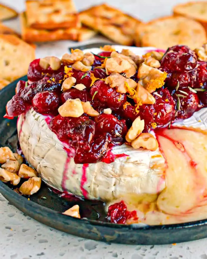 Melted baked brie topped with cranberries and walnuts on a mini cast iron skillet. 