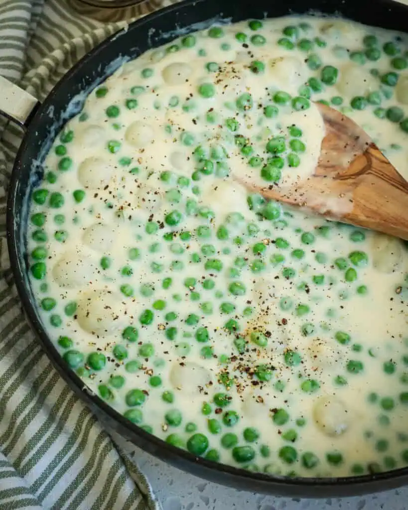 A large skillet full of creamed peas and pearl onions. 