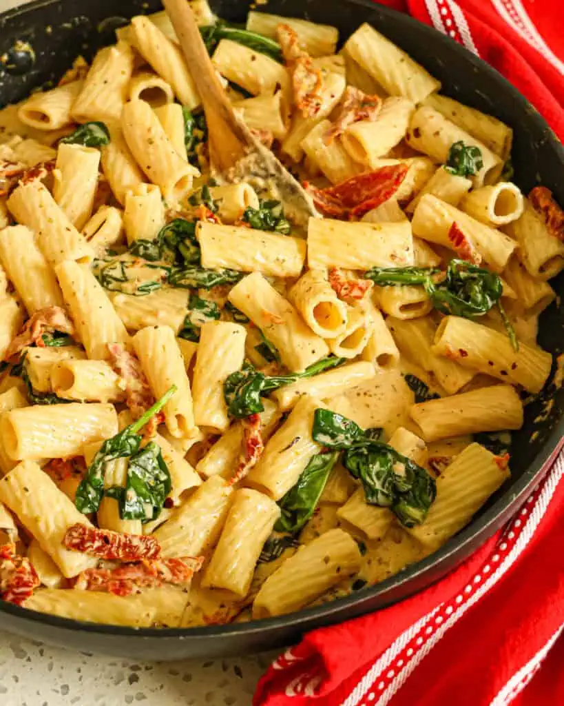 A large skillet full of sundried tomatos pasta with spinach and garlic. 