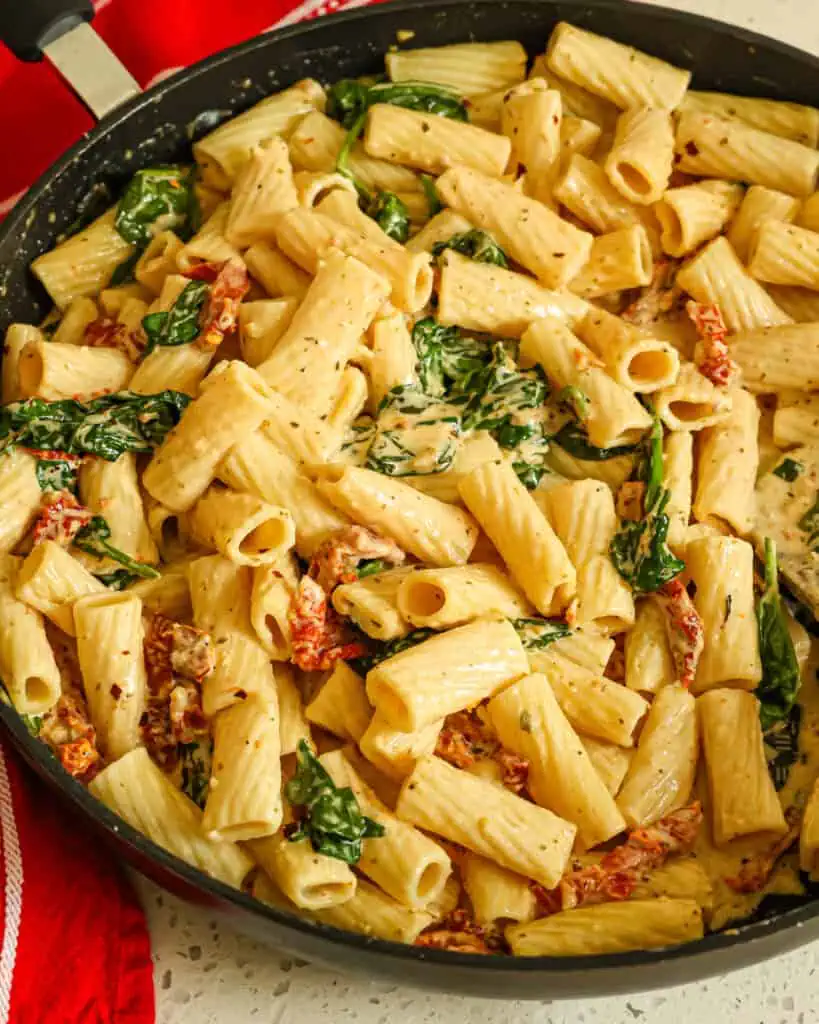 A large skillet of creamy sundried tomato pasta with spinach and garlic. 