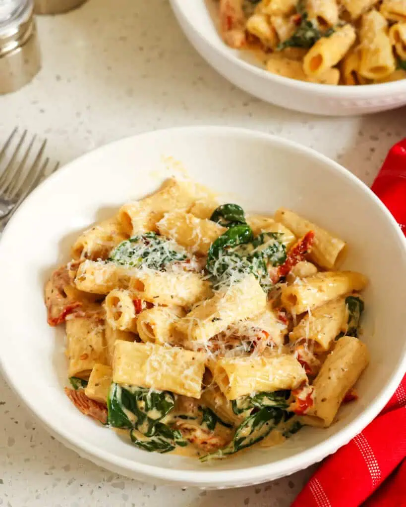 Two bowls full of sundried tomato pasta with forks and salt and pepper shakers on the side. 