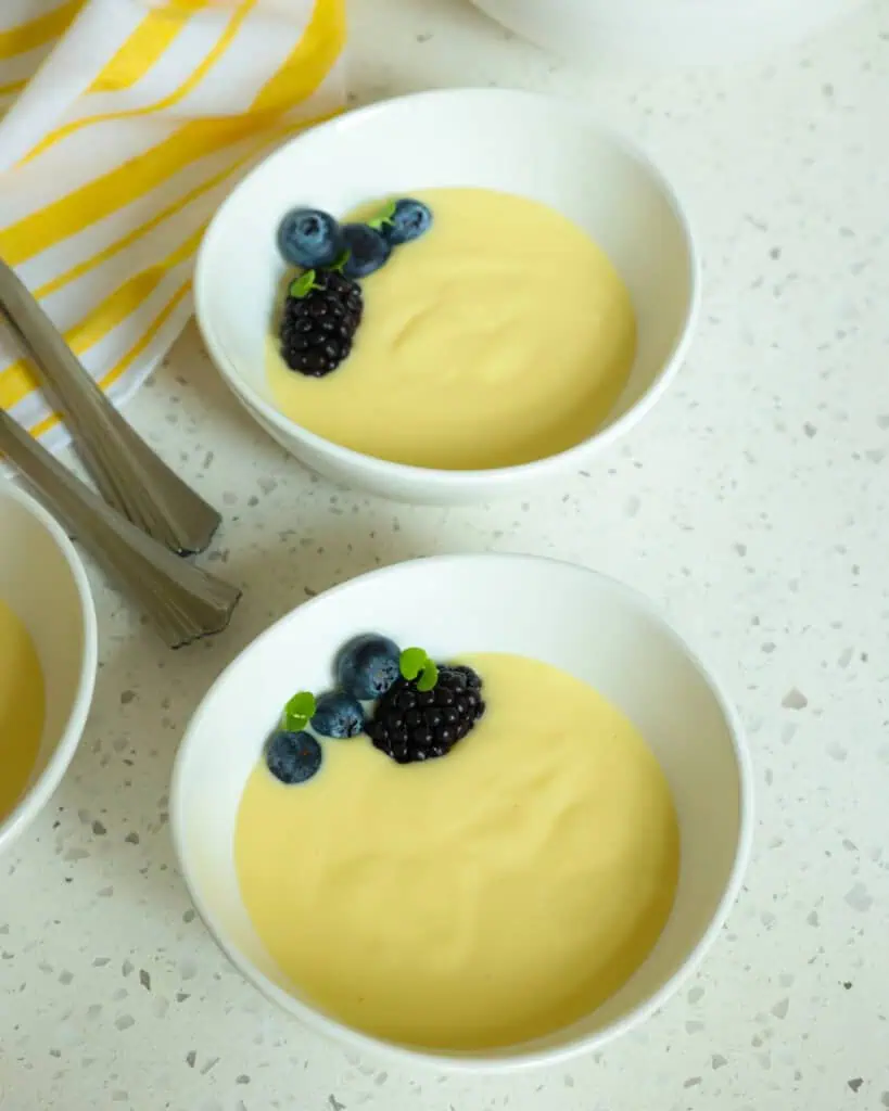 Two smal bowls full of vanilla custard with spoons and a kitchen towel in the background. 