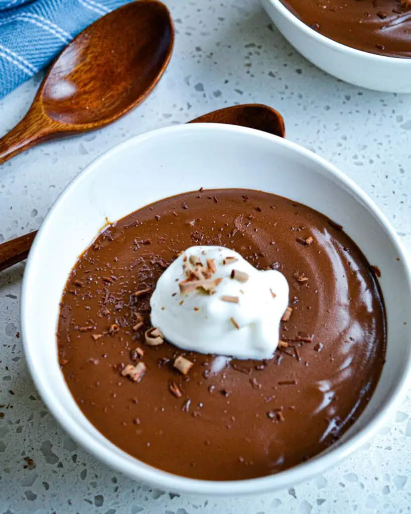 Two bowls of chocolate pudding with whipped cream and chocolate shavings. 