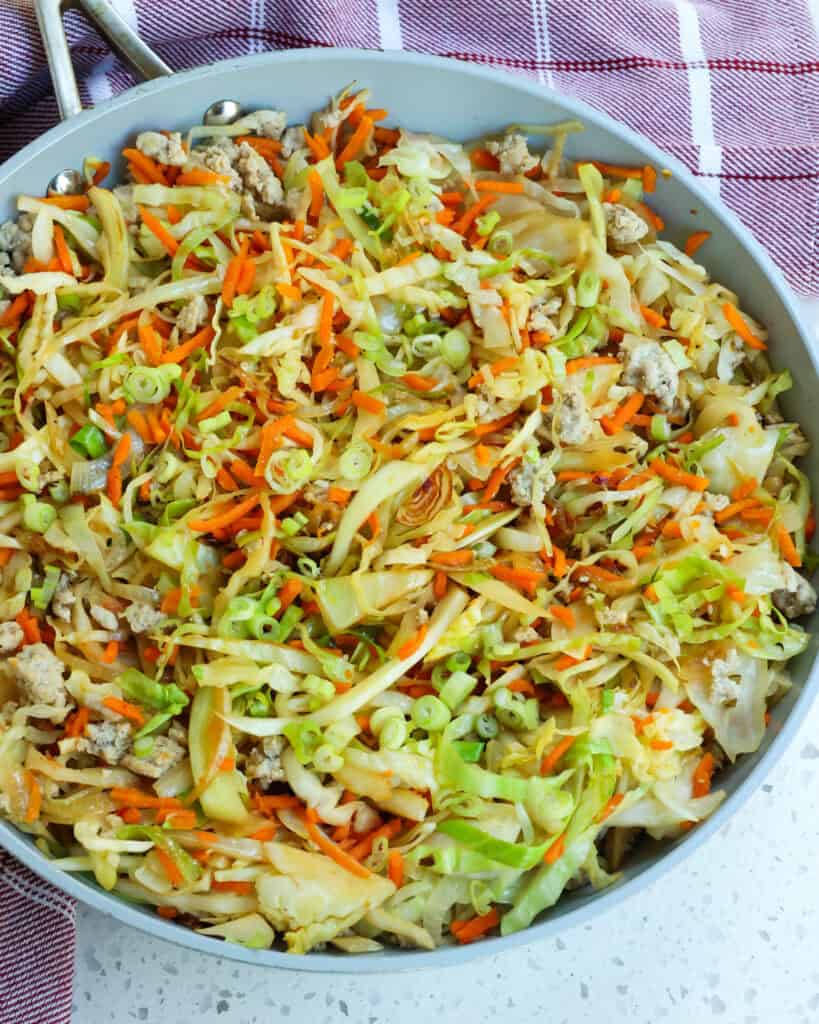 A skillet full of stir fried cabbage with  onions, carrots, and ground turkey. 