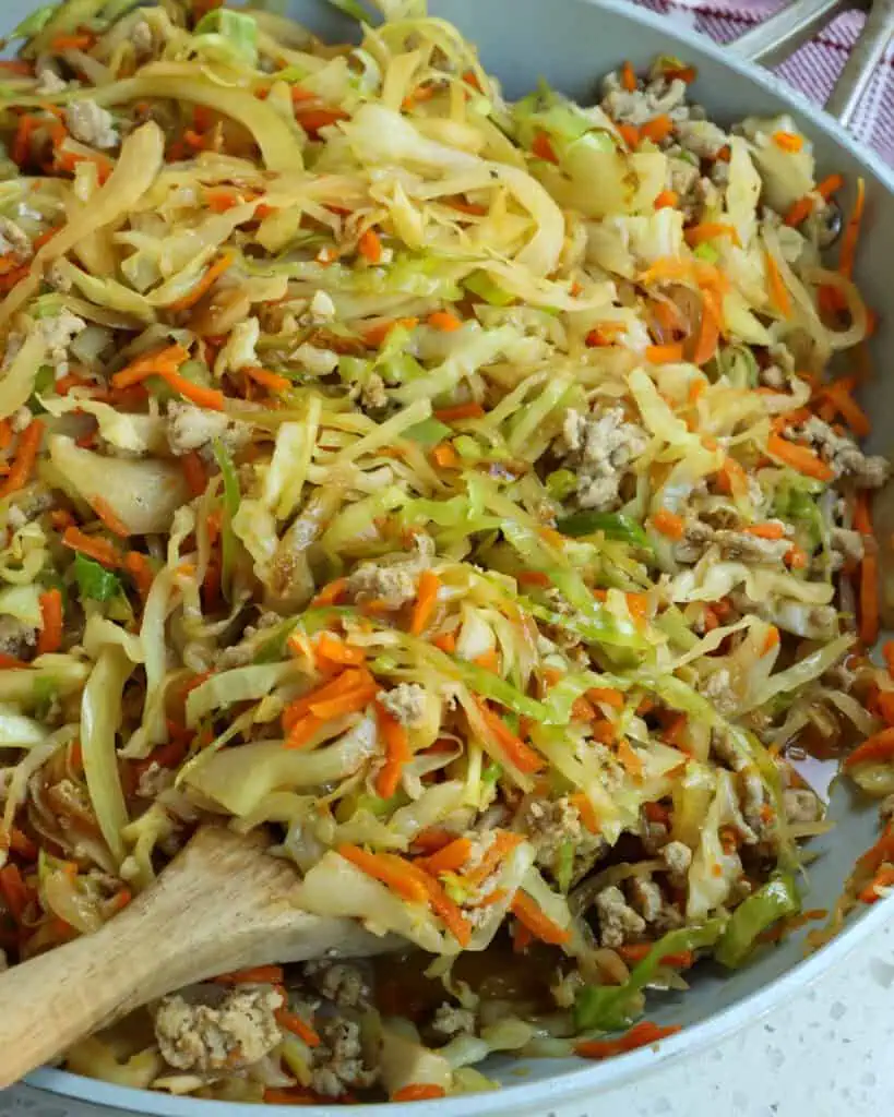 A skillet and a large wooden spoon full of cabbage stir fry.