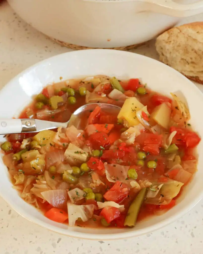 A single serving bowl with a spoon in it full of vegetable soup. 