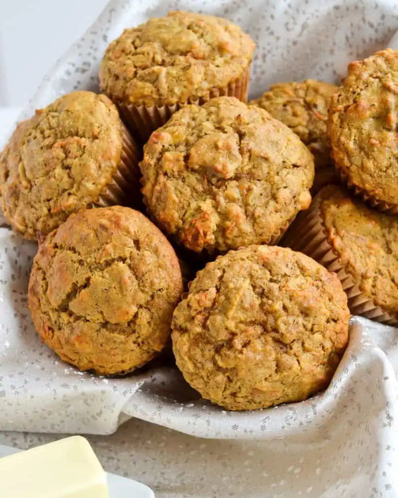 A basket full of fresh baked bran muffins with butter in the foreground. 