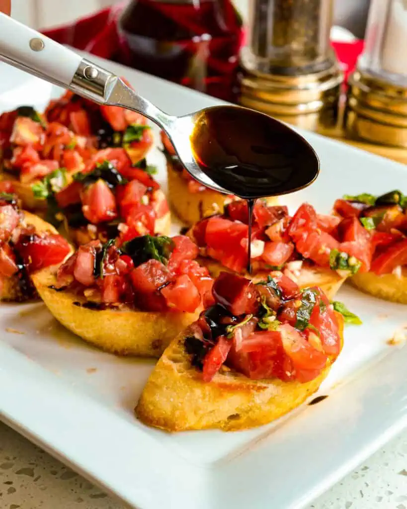 Balsamic glaze being drizzled over bruschetta. 