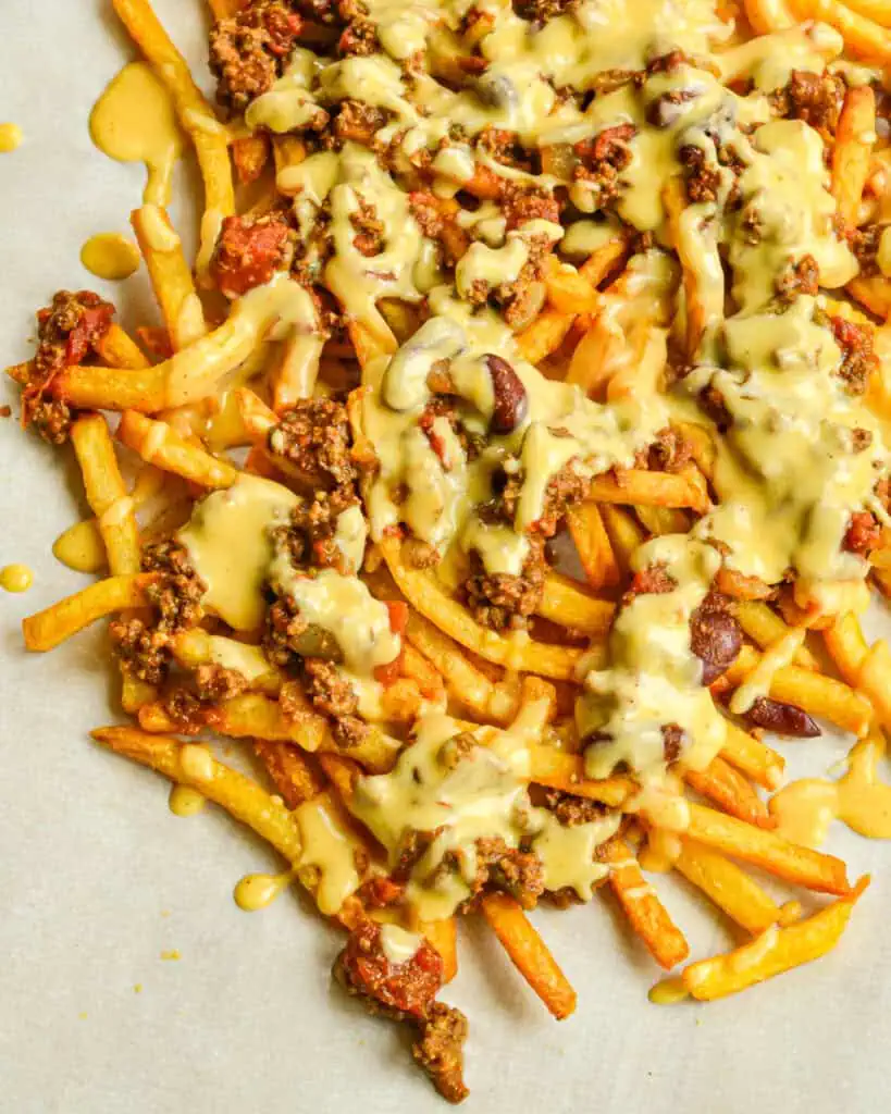 A batch of chili cheese fries on a parchment paper covered serving board. 