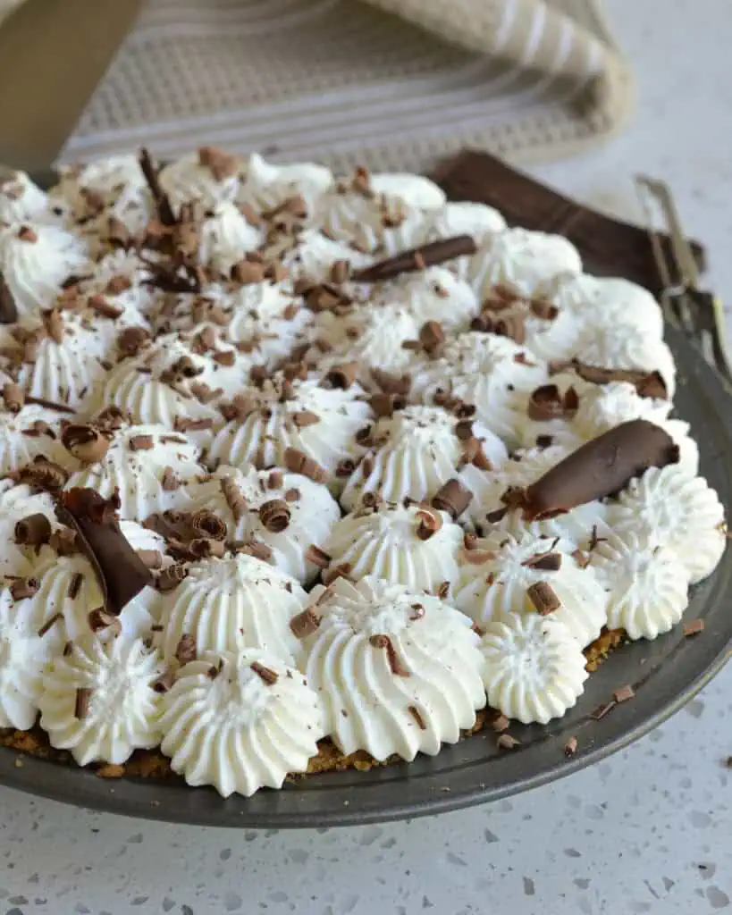 A metal pie tin full of chocolate cream pie with homemade whipped cream and chocolate shavings. 