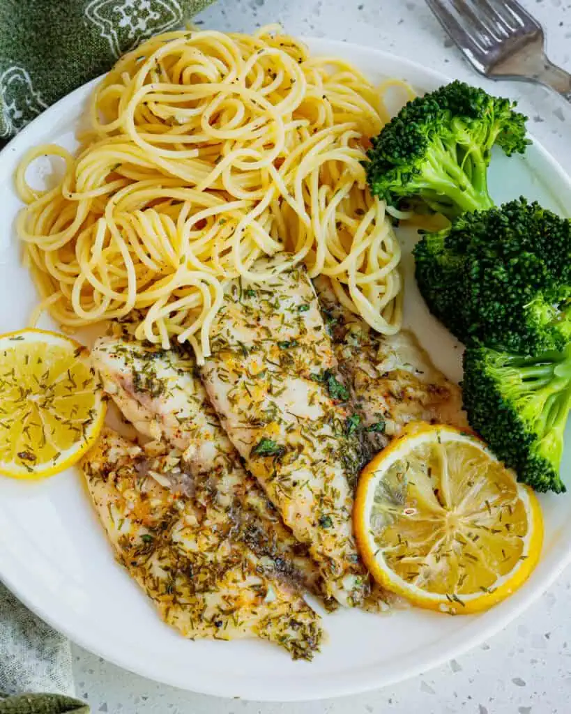 A serving plate with lemon dill baked tilapia, spaghetti noodles, and broccoli. 