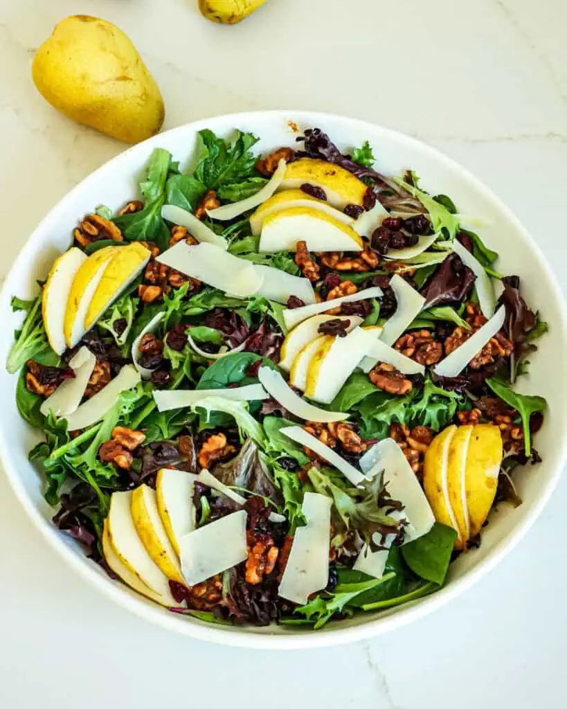 A serving bowl full of pear salad with  walnuts, cranberries, and parmesan cheese. 