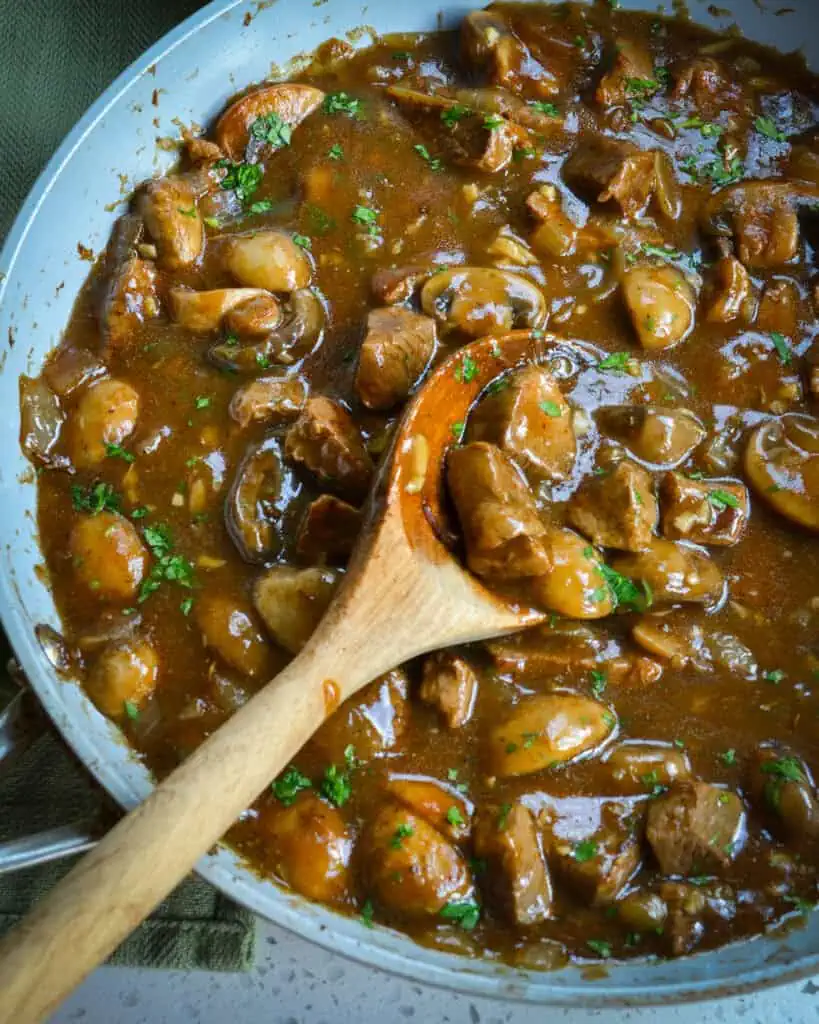 Beef, mushrooms, and gravy in a skillet with a wooden spoon. 