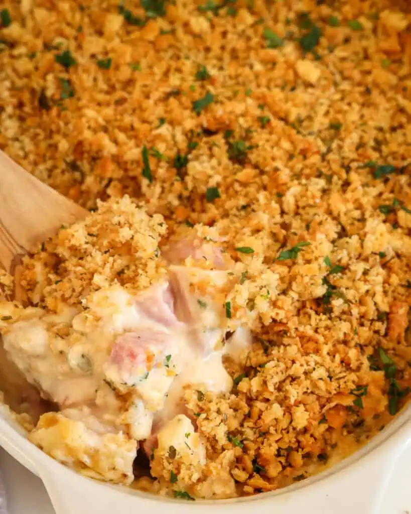 Chicken cordon blue casserole on a wooden spoon in a casserole dish full of chicken cordon blue. 