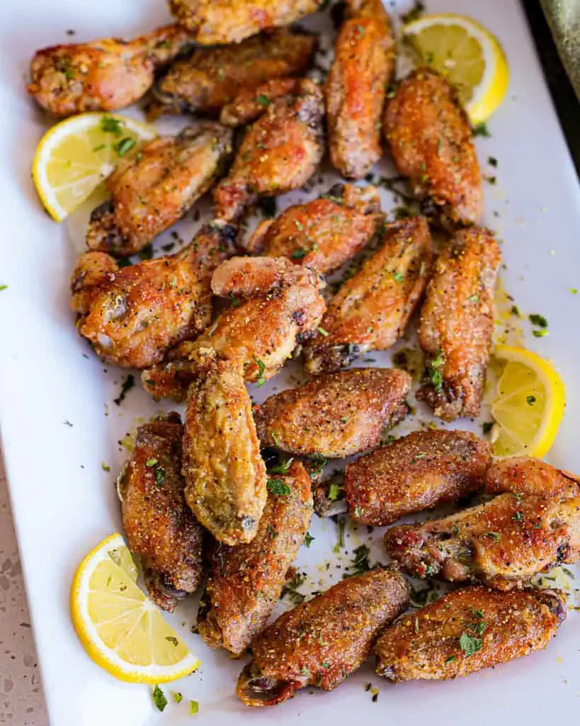 Lemon peppr chicken wings on a serving platter with lemon slices. 