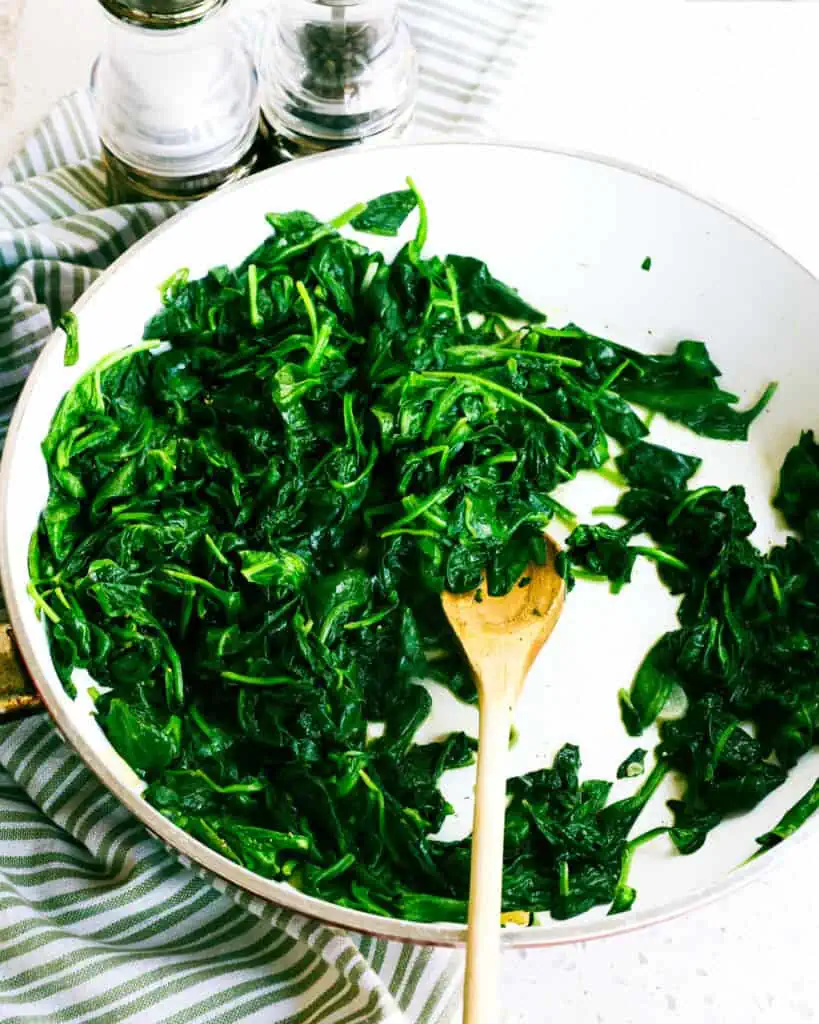 A large skillet full of sauteed spinach with salt and pepper shaker in the background. 