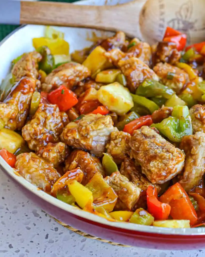 A skillet full of crispy breaded pan fried pork tenderloin bites combined with sweet bell peppers and pineapple in a ginger Asian sauce.