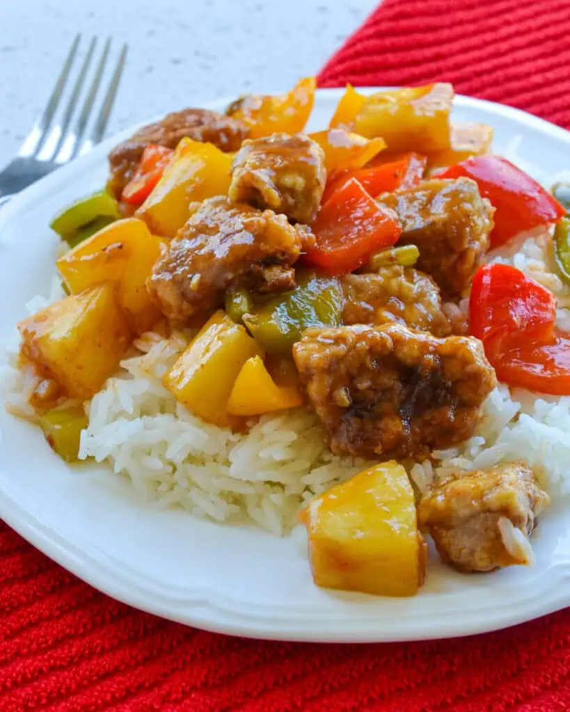 An overhead view of sweet and sour pork over rice on a plate with a fork in the background. 