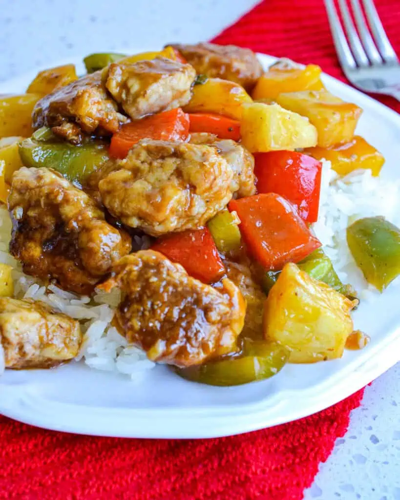 Sweet and sour pork over white rice on a single serving plate with a fork in the background. 