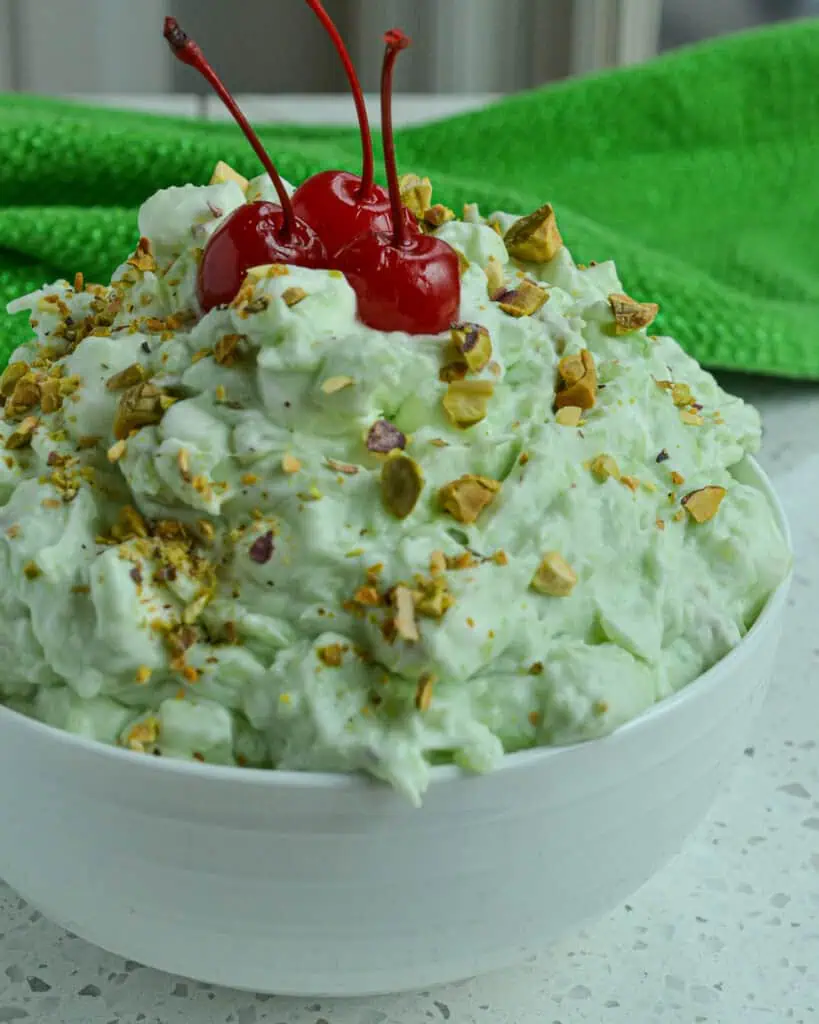 A bowl full of watergate salad with chopped pistachios and maraschino cherries. 