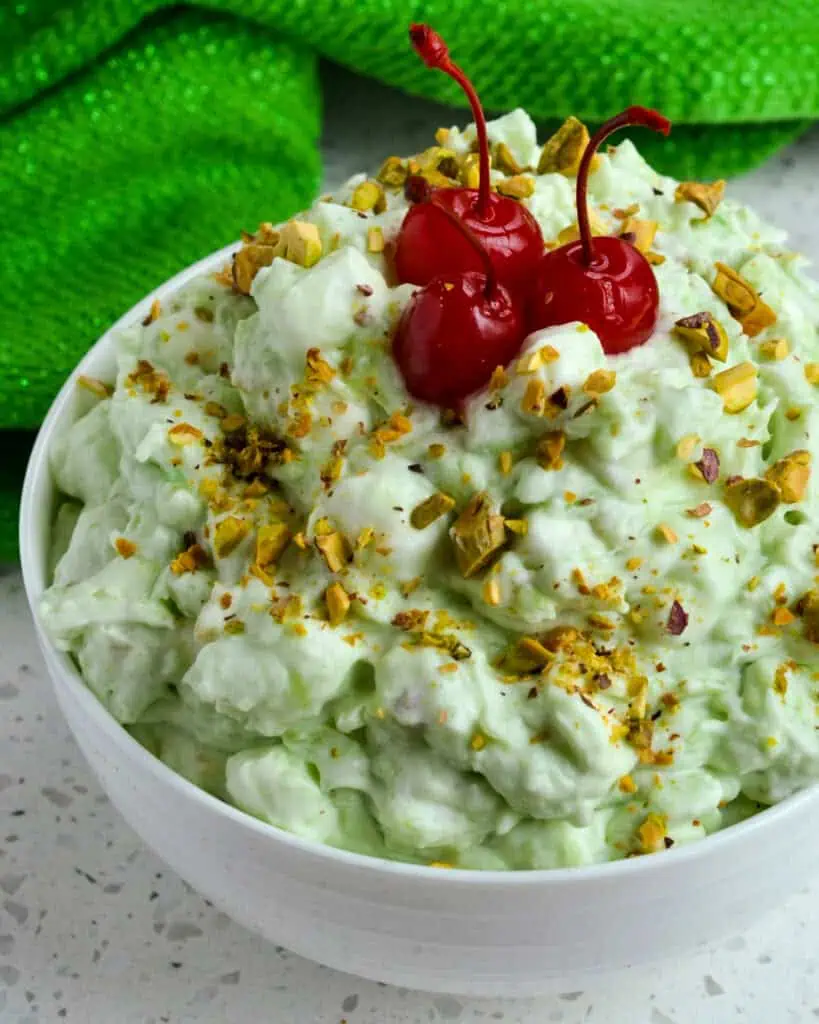 A while bowl full of watergate salad garnish with chopped pistachios and maraschino cherries. 