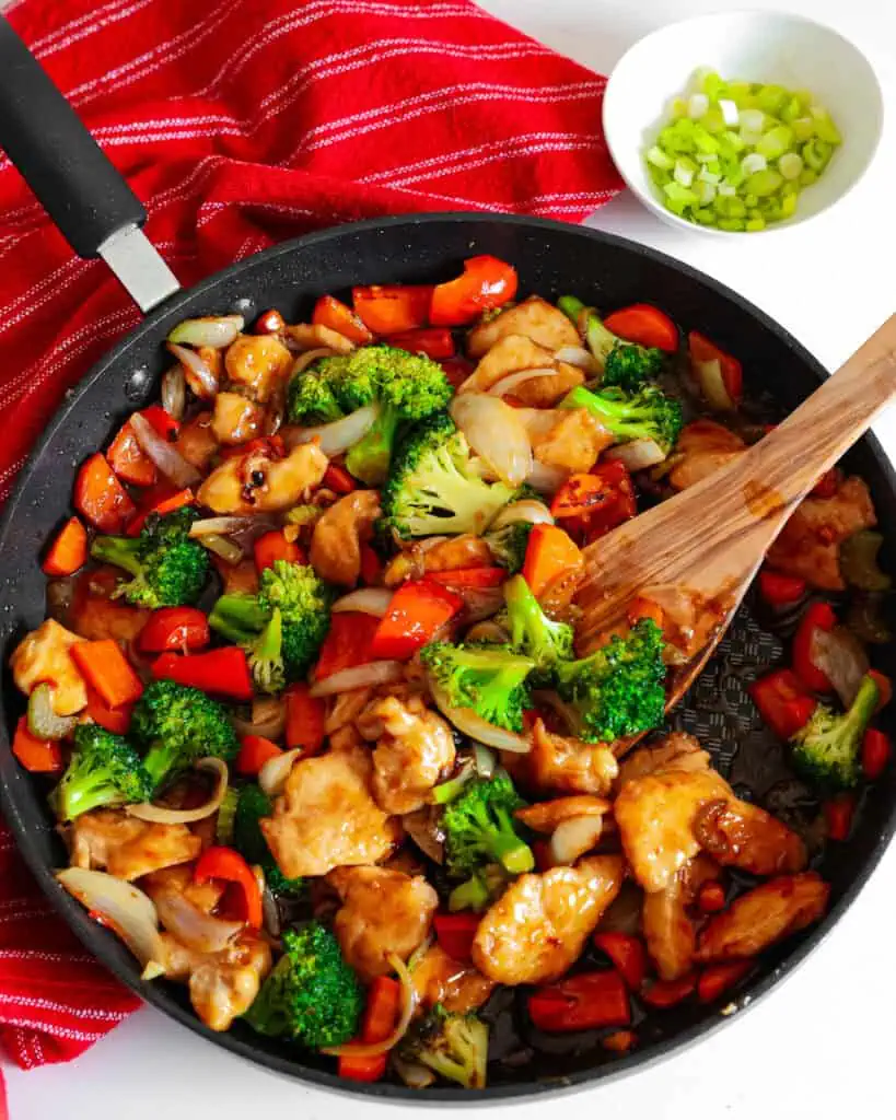 An overhead view of hunan chicken in a large skillet with a wooden spatula. 